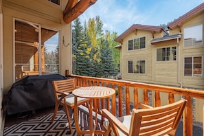 A wooden deck with a table and chairs, a grill, and a view of neighboring houses and trees. - Central Park 22- New Listing! Luxury Condo Great Location Close to Ski Lift (Ketchum)
