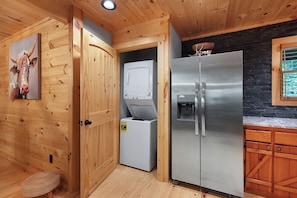 Eine kleine Küche mit Holzwänden, einem Kühlschrank, einer Waschmaschine und einem Fenster mit Blick.
