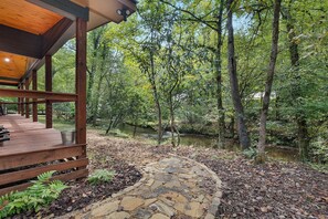 A wooden deck with a stone pathway leading to a river, surrounded by dense forest. - Creekside Haven - Fightingtown Creek Cabin in Cherry Log (Cherry Log)