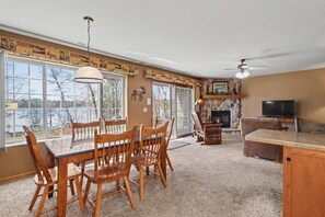 Ein großzügiges Wohnzimmer mit Kamin, Fernseher und Essbereich mit Holzsesseln und Tisch.