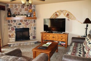 Ein Wohnzimmer mit Kamin aus Stein, einem Flachbildfernseher, einem Holztisch und einer Couch mit gemusterten Kissen.
