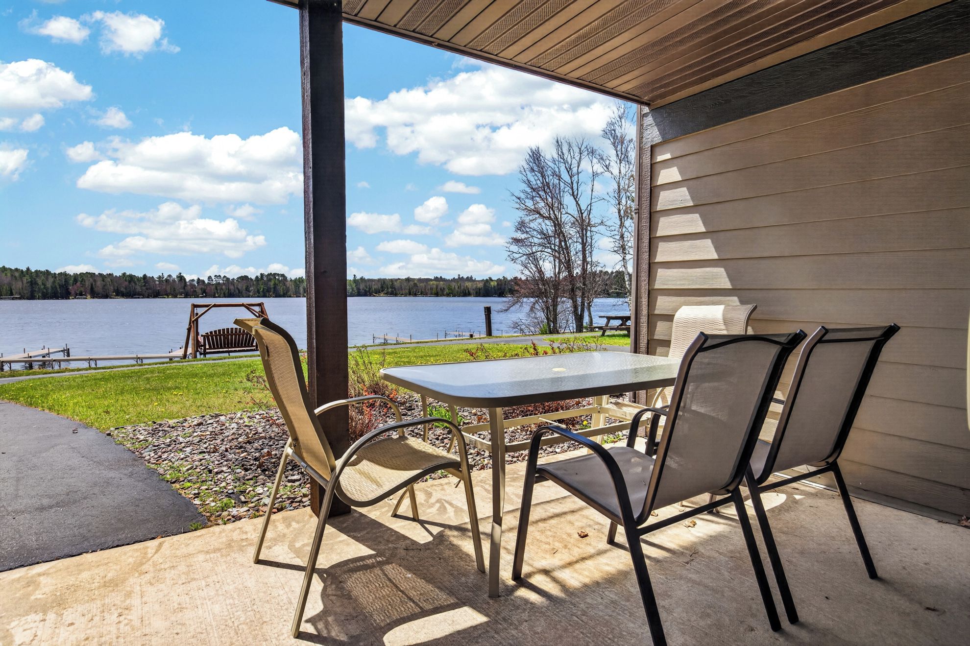 Une terrasse extérieure avec une table et des chaises, donnant sur un lac avec un quai et une balançoire.
