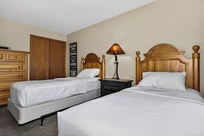 A hotel room with two single beds, a wooden wardrobe, a nightstand with a lamp, and a wall with a motivational quote. - Eagle River Chain Condo with Indoor Pool and Jacuzzi! (Eagle River)