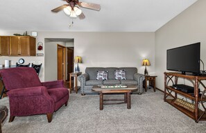 A living room with a red armchair, grey sofa, wooden coffee table, and a television on a wooden stand. - Eagle River Chain Condo with Indoor Pool and Jacuzzi! (Eagle River)