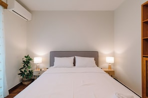 A hotel room with a large bed, two bedside lamps, a potted plant, and an air conditioning unit. - Sophia • Elegant Penthouse at Central Glyfada 120sqm Private Terrace (Glifada)
