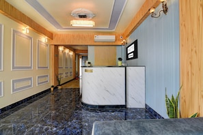 A hotel reception area with a marble reception desk, a reception sign, and a wall-mounted sign indicating the hotel name.