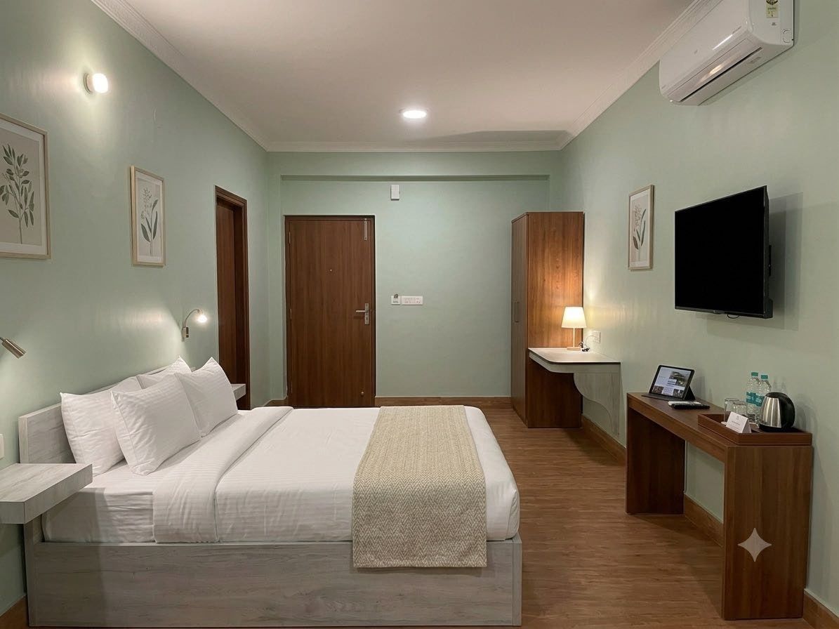 A hotel room with a bed, bedside table, desk, TV, and a wardrobe.