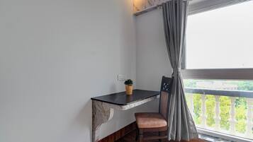 Habitación de esquina con escritorio de mármol, una silla, planta en maceta y vista a la vegetación desde un balcón.