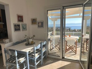 A room with a dining table and chairs, a sliding glass door leading to an outdoor patio with a view of the sea. - Country House 'Iron Hill Villa' with Sea View, Wi-Fi and Air Conditioning (Κρανίδι)