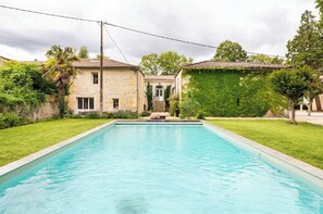 A swimming pool with a stone building in the background, surrounded by greenery. - Italian-style villa by the river, near Bordeaux (Quinsac)