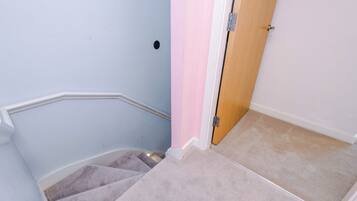 Un escalier recouvert de moquette avec une main courante, une porte en bois et un mur muni d’une seule prise électrique.