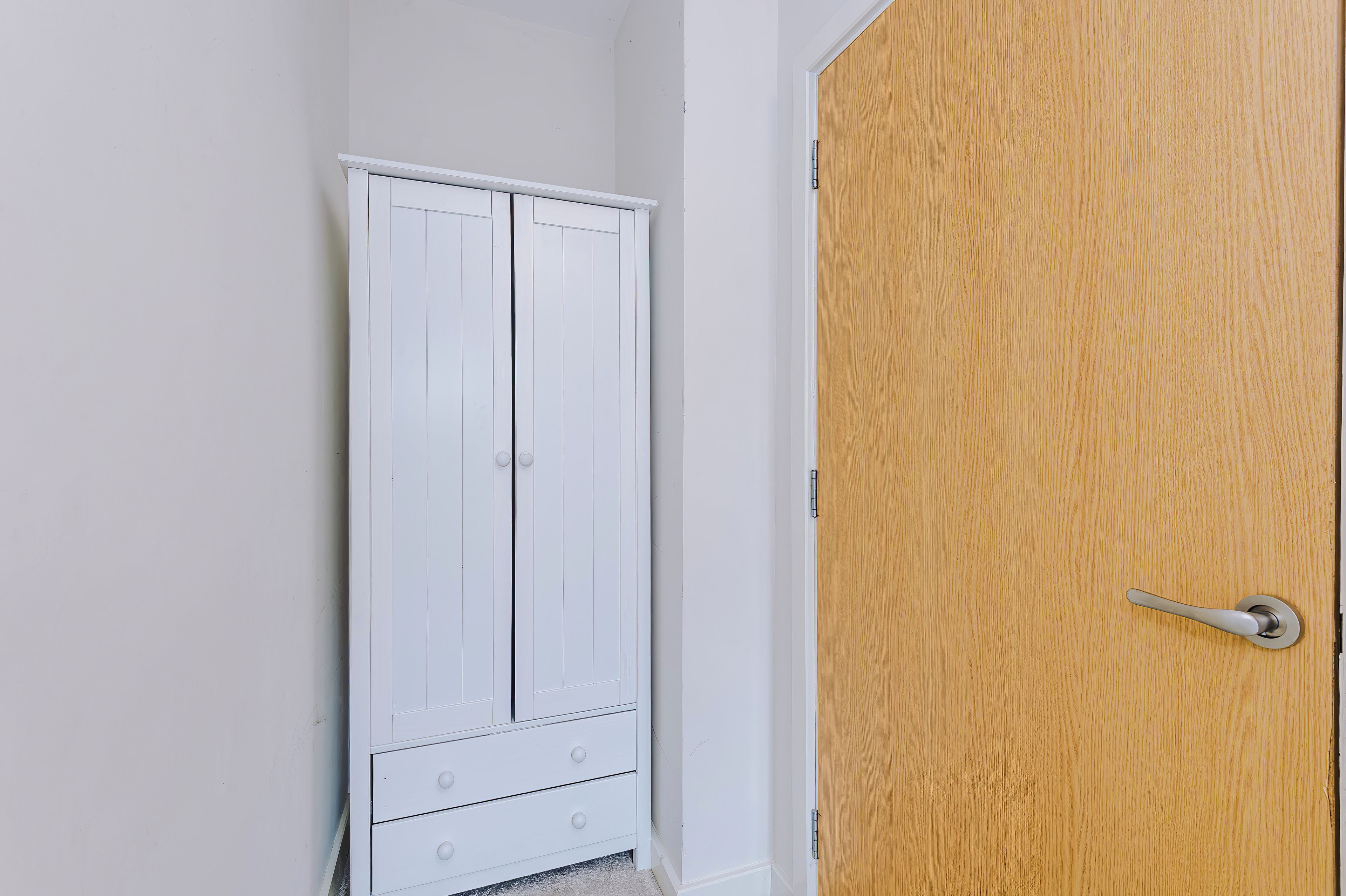 Une armoire blanche avec deux tiroirs et une porte en bois dotée d’une poignée.