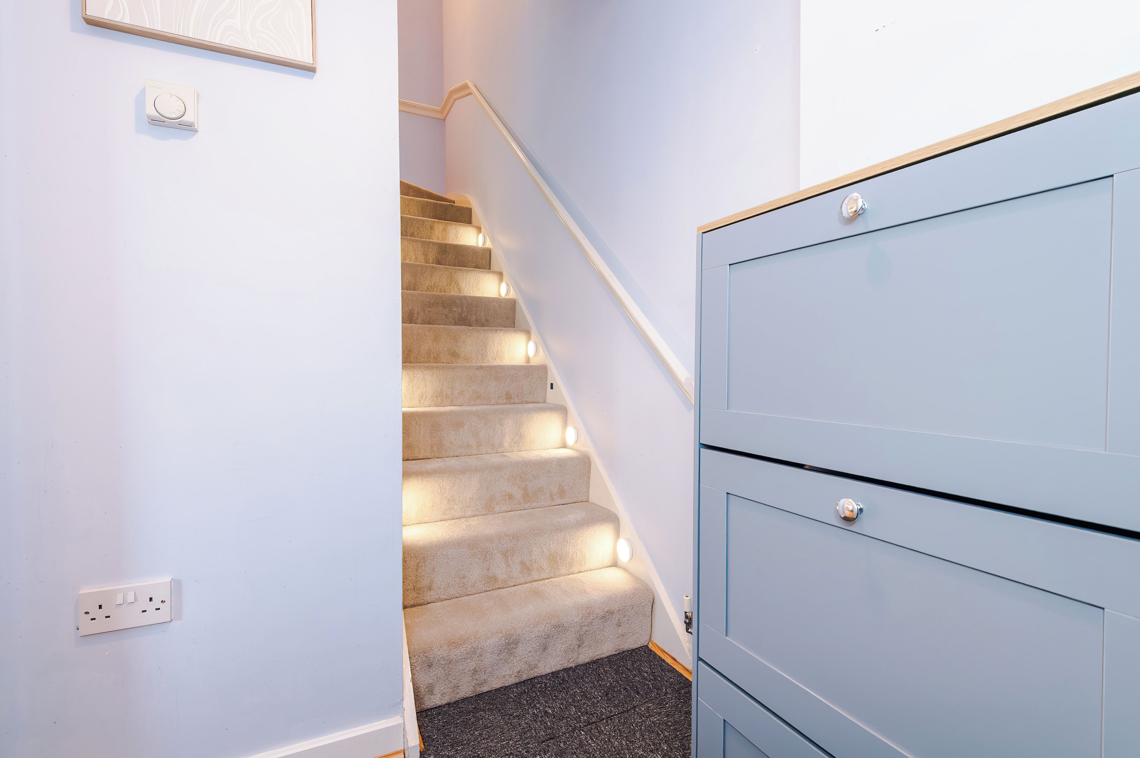 A carpeted staircase with a handrail, a light switch, and a blue cabinet with a handle.