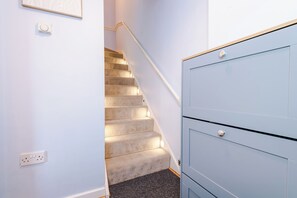 Ein Teppichbelag bedecktes Treppenhaus mit Geländer, einem Lichtschalter und einem blauen Schrank mit Griff.