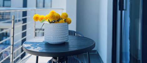 Een balkon met een ronde tafel, een stoel en een witte vaas met gele bloemen.