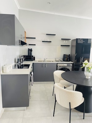 A modern kitchen with grey cabinets, a black countertop, and a round dining table with chairs.