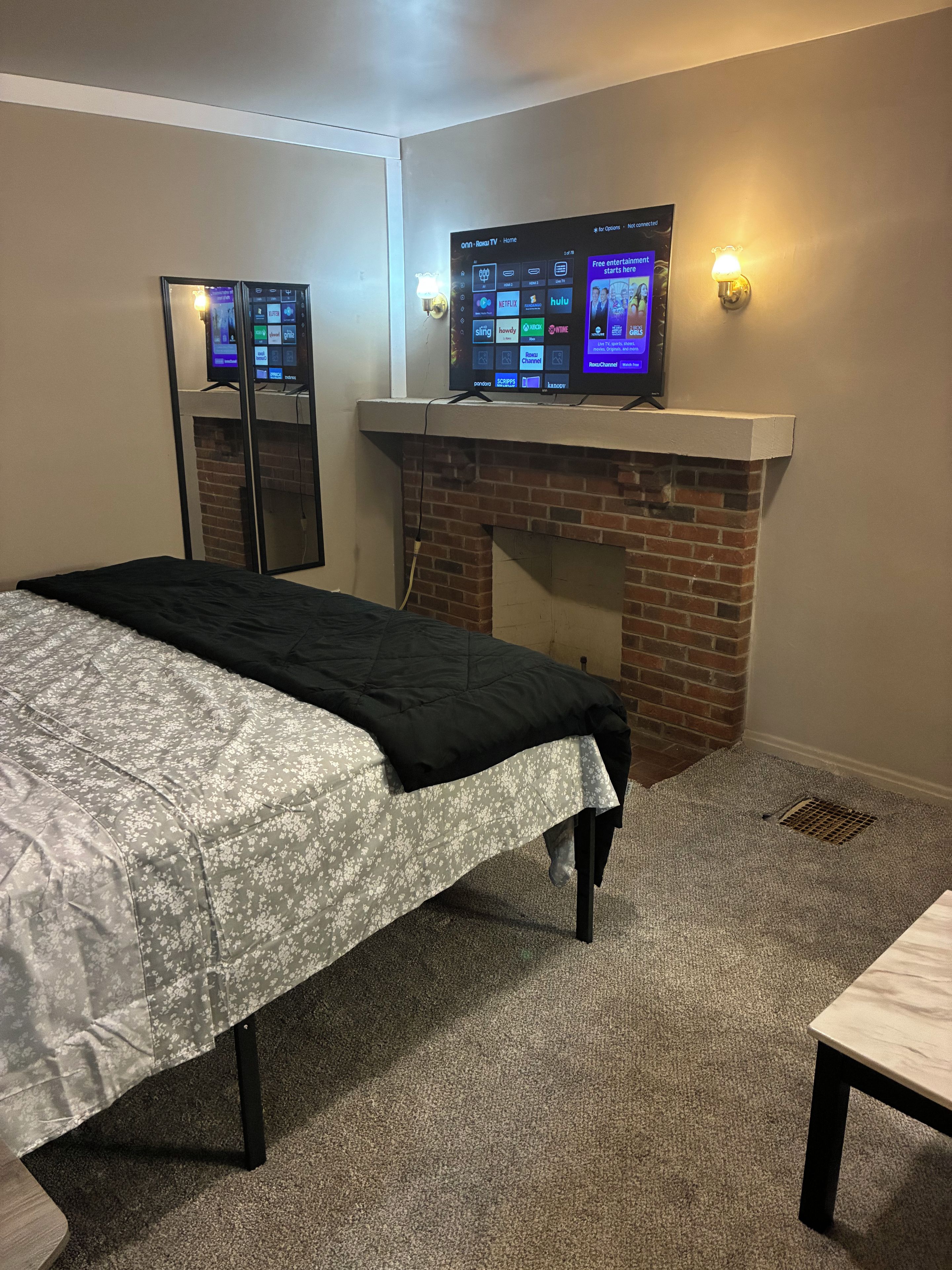 A hotel room with a bed, a television mounted on the wall, and a brick fireplace.