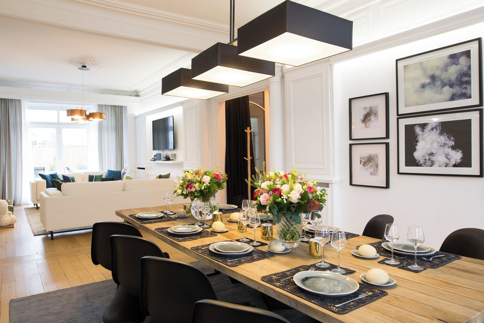Un espace repas avec une longue table dressée pour six personnes, entourée de chaises noires.