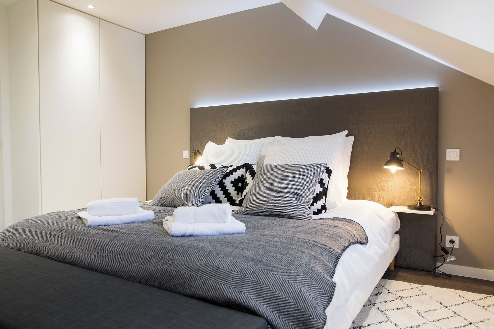 Une chambre moderne avec un grand lit, de nombreux oreillers, une table de chevet avec une lampe et un luminaire fixé au mur.