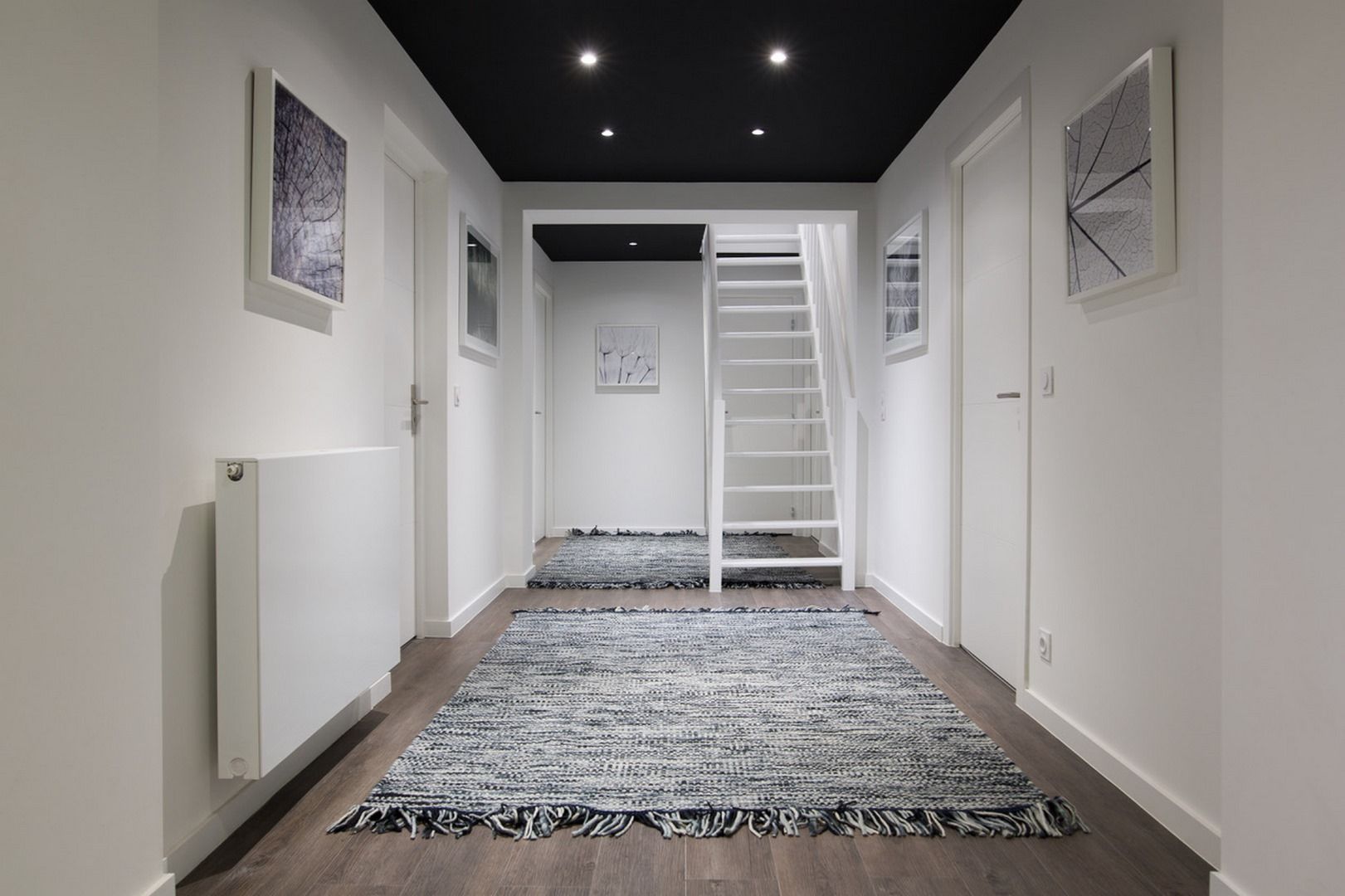 Un couloir avec un escalier, des murs blancs et un tapis à motifs.