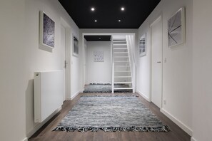 Un couloir avec un escalier, des murs blancs et un tapis à motifs.