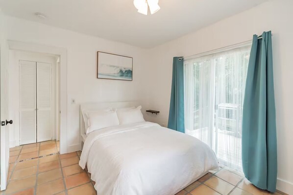 Une chambre à coucher avec un lit, une fenêtre avec des rideaux, une porte et un tableau accroché au mur.