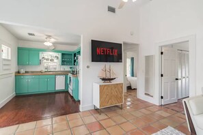 Et moderne køkken med skånsomt blå skabe, en hvid bordplade og en lille ø med en skibsmodel. Et fladskærms-tv på væggen viser 'NETFLIX'.