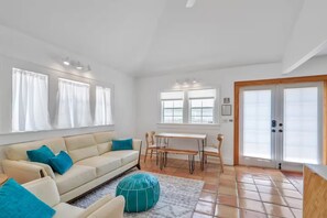 A spacious living area with a sofa, a dining table, and chairs. There are large windows with curtains, a tiled floor, and a door with a handle. - Iconic Coastal retreat close to Siesta Key Beach! (Sarasota)