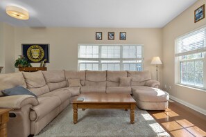 A living room with a sectional sofa, a wooden coffee table, and a lamp. - Fighting Irish Retreat | 3BR/4BA (South Bend)