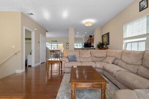 A spacious living room with a large beige sectional sofa, a wooden coffee table, and a dining area with a table and chairs. - Fighting Irish Retreat | 3BR/4BA (South Bend)