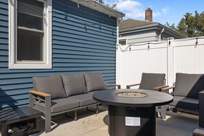 An outdoor seating area with a sofa and chairs, a round table with a fire pit, and a window with blinds. - 3BR/1BA Updated South Bend Retreat Close to ND (South Bend)