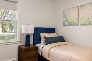 Un dormitorio con una cama, una mesita de noche, una lámpara y dos cuadros colgados en la pared.