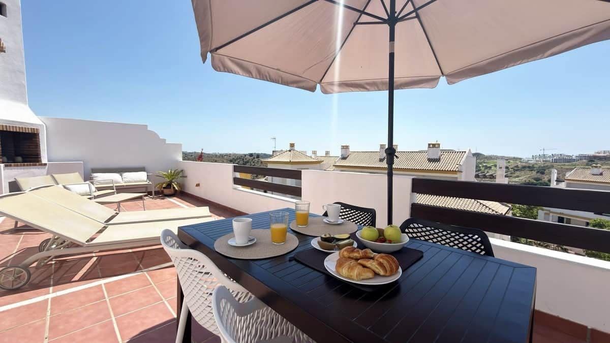A rooftop terrace with a table set for breakfast, including croissants, fruit, and a beverage.