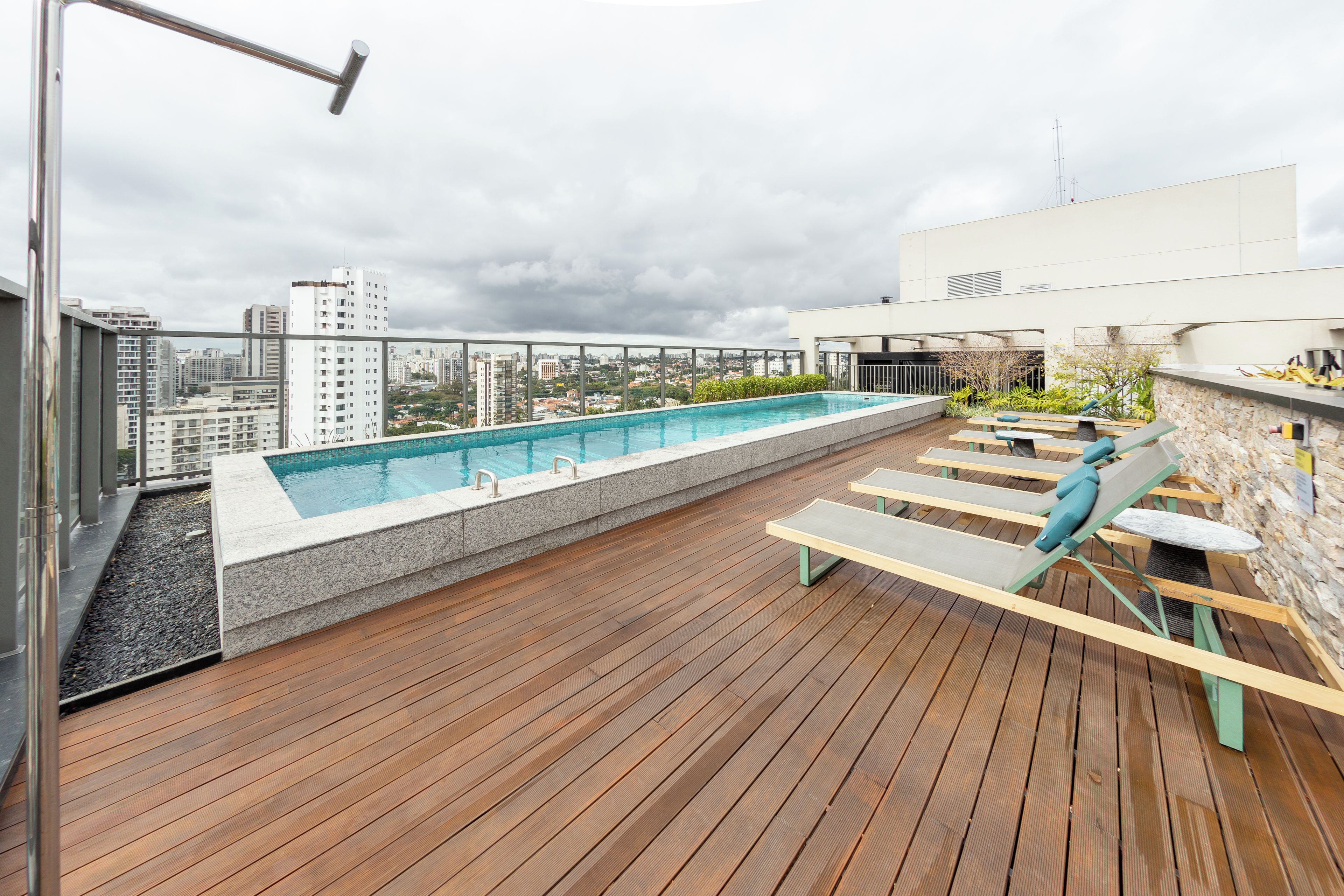 A rooftop pool with a wooden deck, lounge chairs, and a cityscape view.
