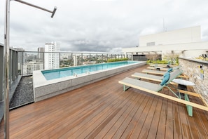 A rooftop pool with a wooden deck, lounge chairs, and a cityscape view. - Balkon by Bhomy (São Paulo)
