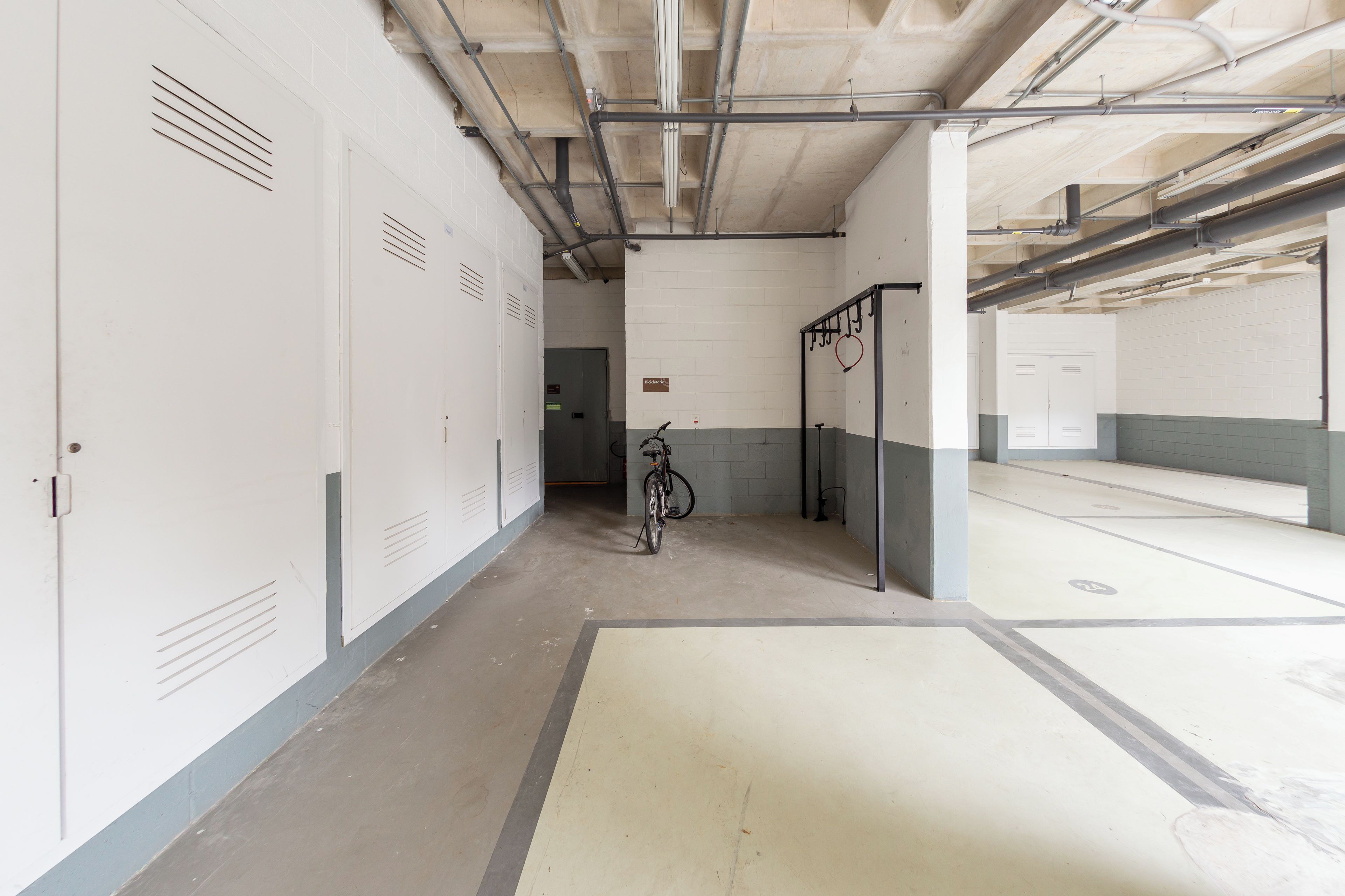 A corridor with lockers, a bicycle, and a door leading to a parking area.