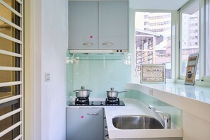 A compact kitchen with two gas stoves, a stainless steel sink, and a window overlooking a cityscape.
