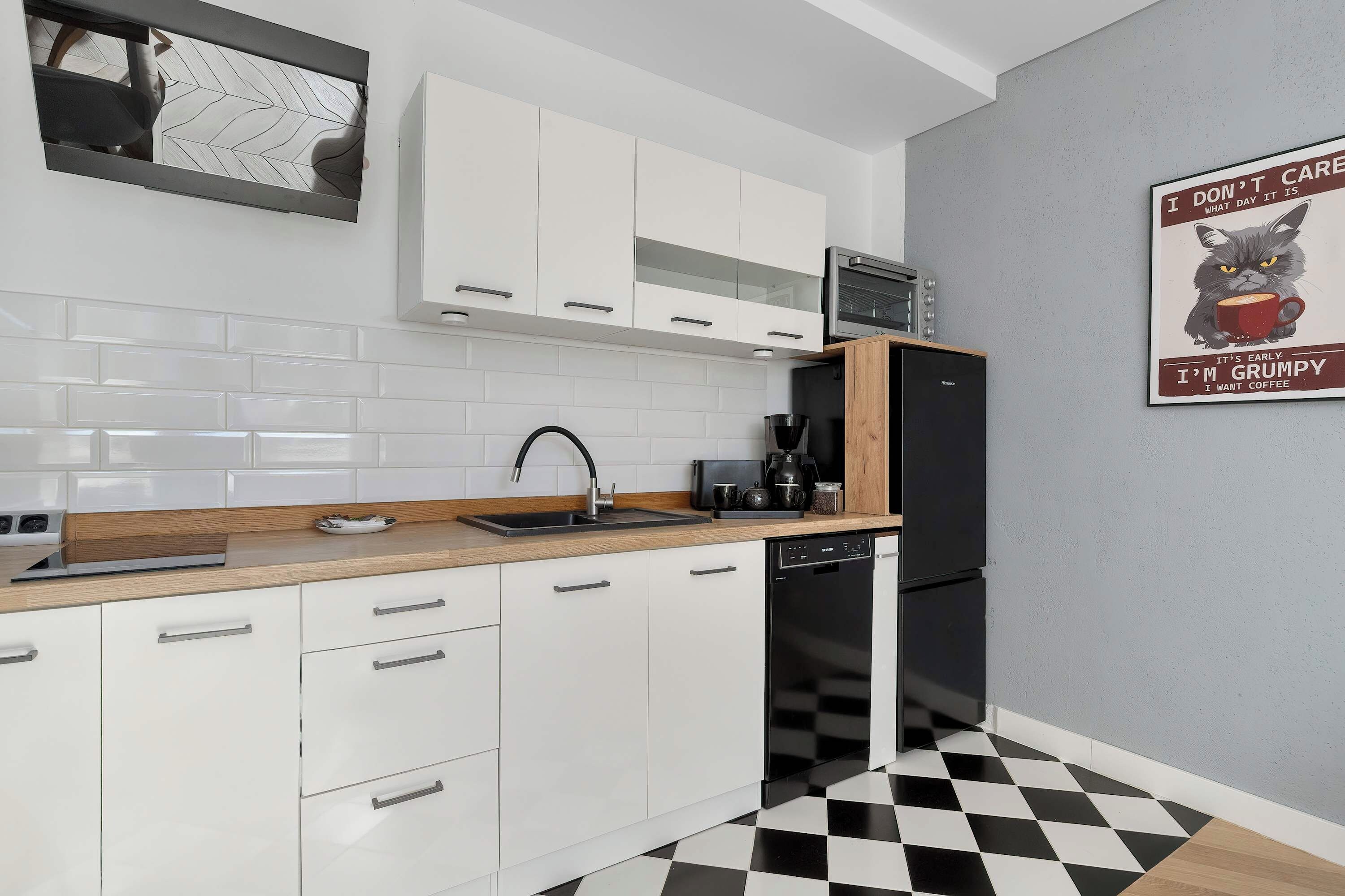 A modern kitchen with white cabinets, a black and white checkered floor, and a coffee-themed poster on the wall.