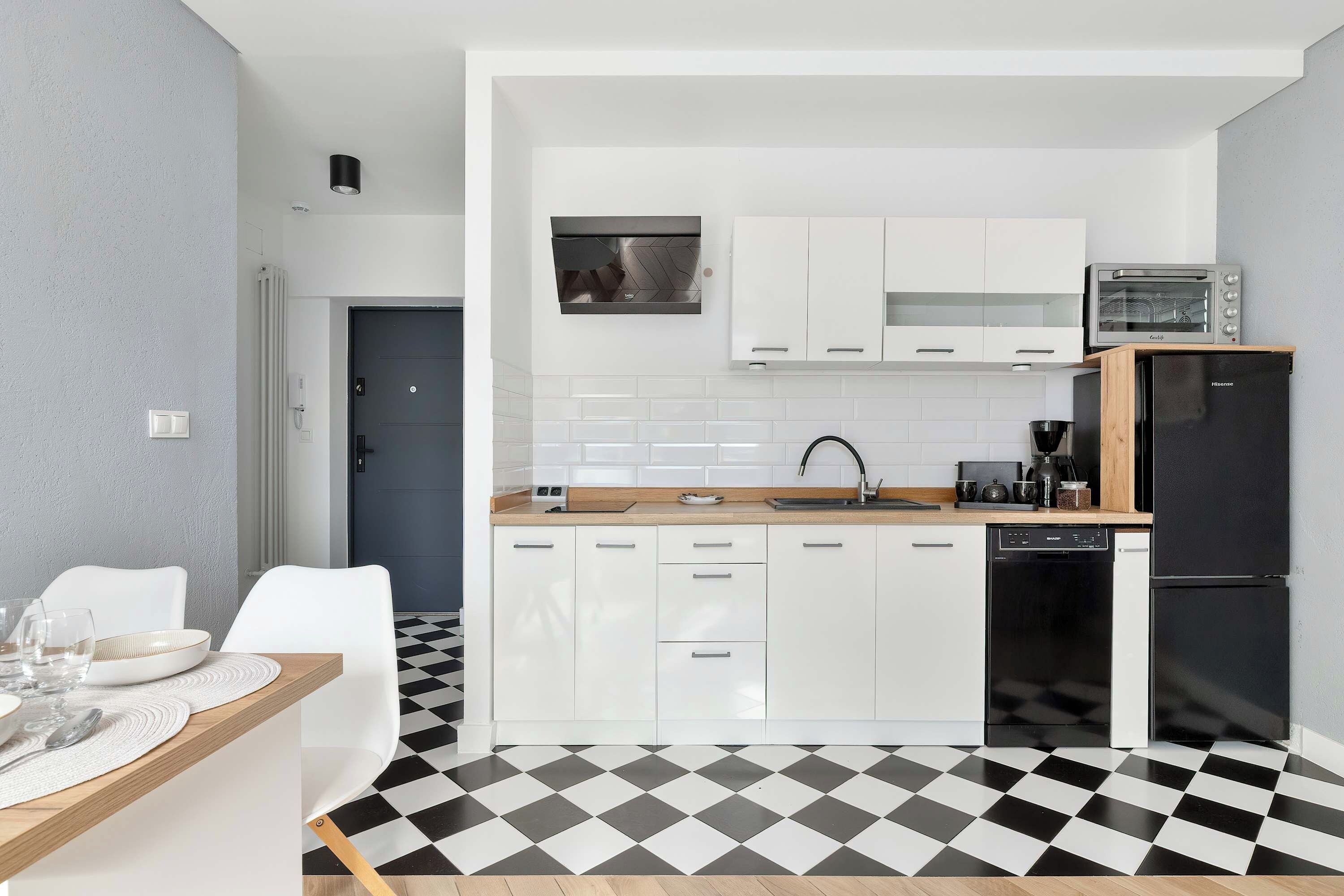 A compact kitchen with white cabinets, a black and white checkered floor, a microwave, a coffee maker, and a dishwasher.