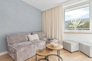 A modern living room with a grey sofa, a round wooden table, and a window with curtains. - Gdynia | 31 Starowiejska | Comfortable Apartment | Centre (Gdynia)