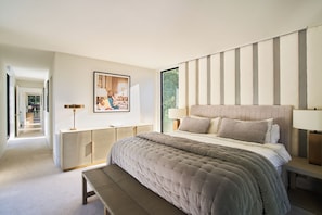 Ein modernes Schlafzimmer mit einem großen Bett, Nachttischen, einer Bank und Blick ins Freie.