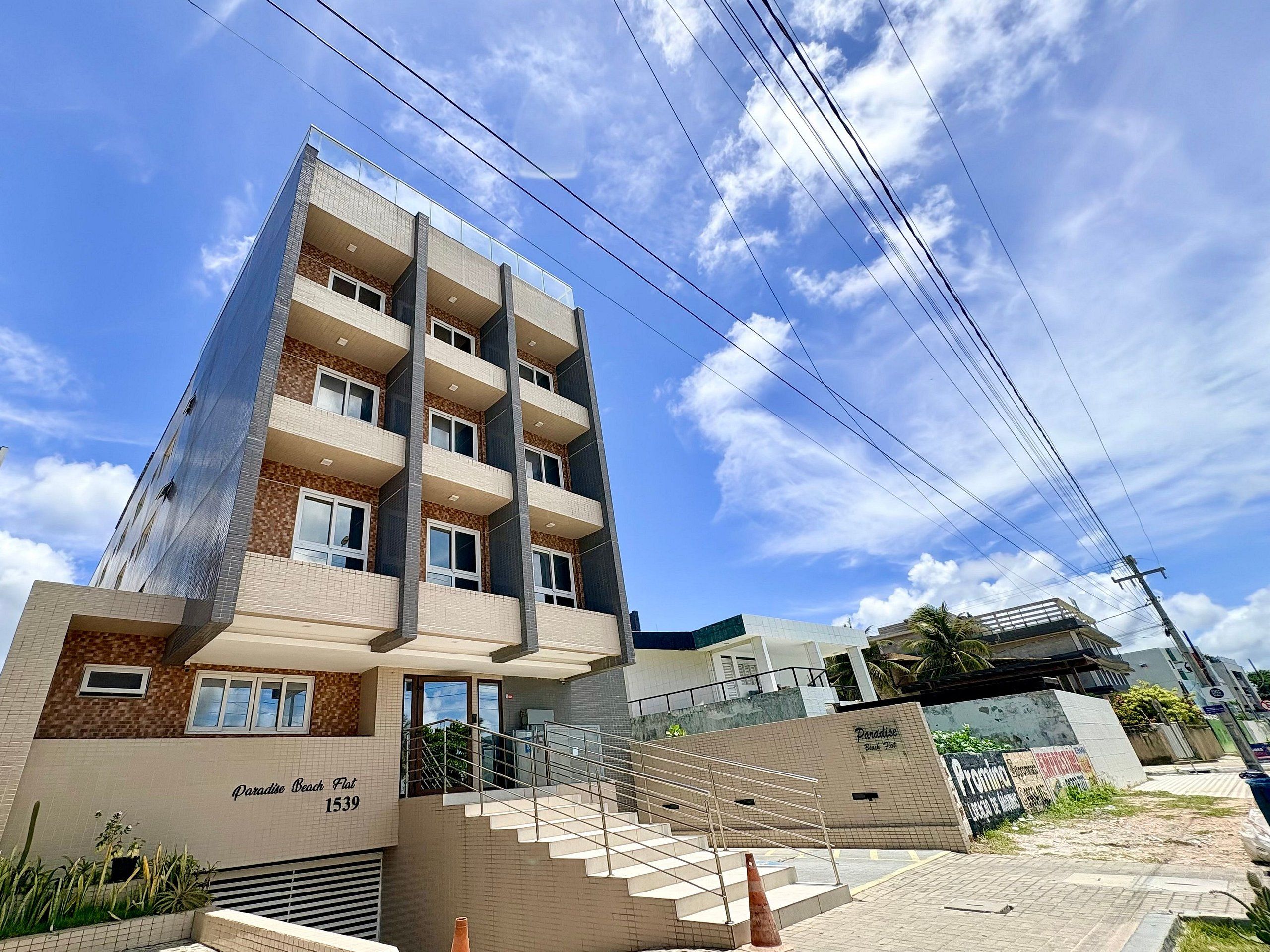 A multi-story building with a flat roof terrace, a staircase leading to the entrance, and a sign indicating 'Paradise Beach Flat 1539'.