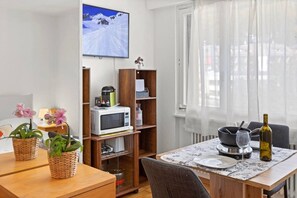 A dining area with a table set for two, a microwave, and a television mounted on the wall. - A studio apartment just a 5-minute walk from the cable cars (Crans-Montana)