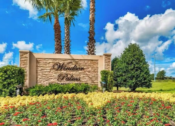 A sign with 'Windor Palms' written on it, surrounded by a garden with various flowers and palm trees. - Apartment*Disney*Universal in Windsor Palms (Kissimmee)