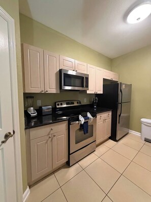 A compact kitchen with beige cabinets, a microwave, a stove, and a refrigerator. - Apartment*Disney*Universal in Windsor Palms (Kissimmee)