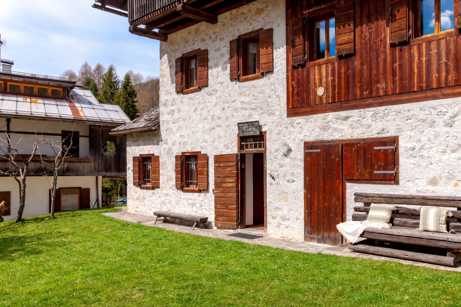 A stone building with wooden shutters, a bench, and a small table in the yard.