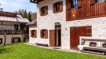 A stone building with wooden shutters, a bench, and a small table in the yard.