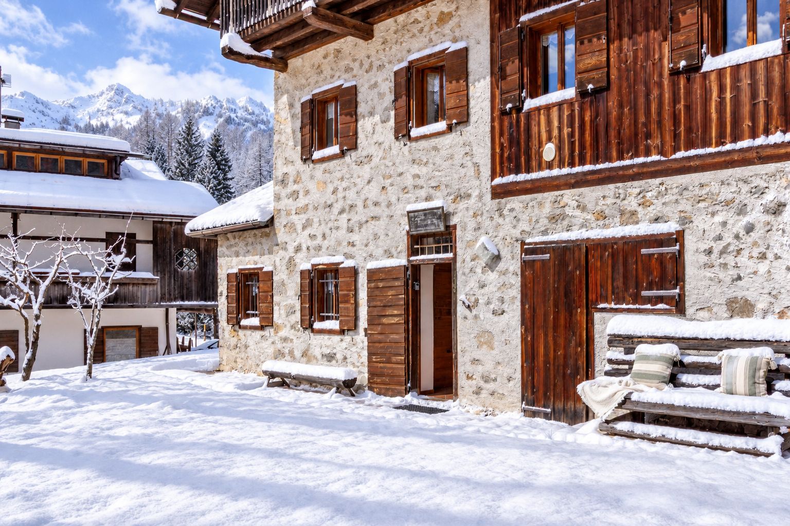 Un bâtiment en pierre avec des volets en bois et un balcon, entouré d’un paysage enneigé et d’arbres.