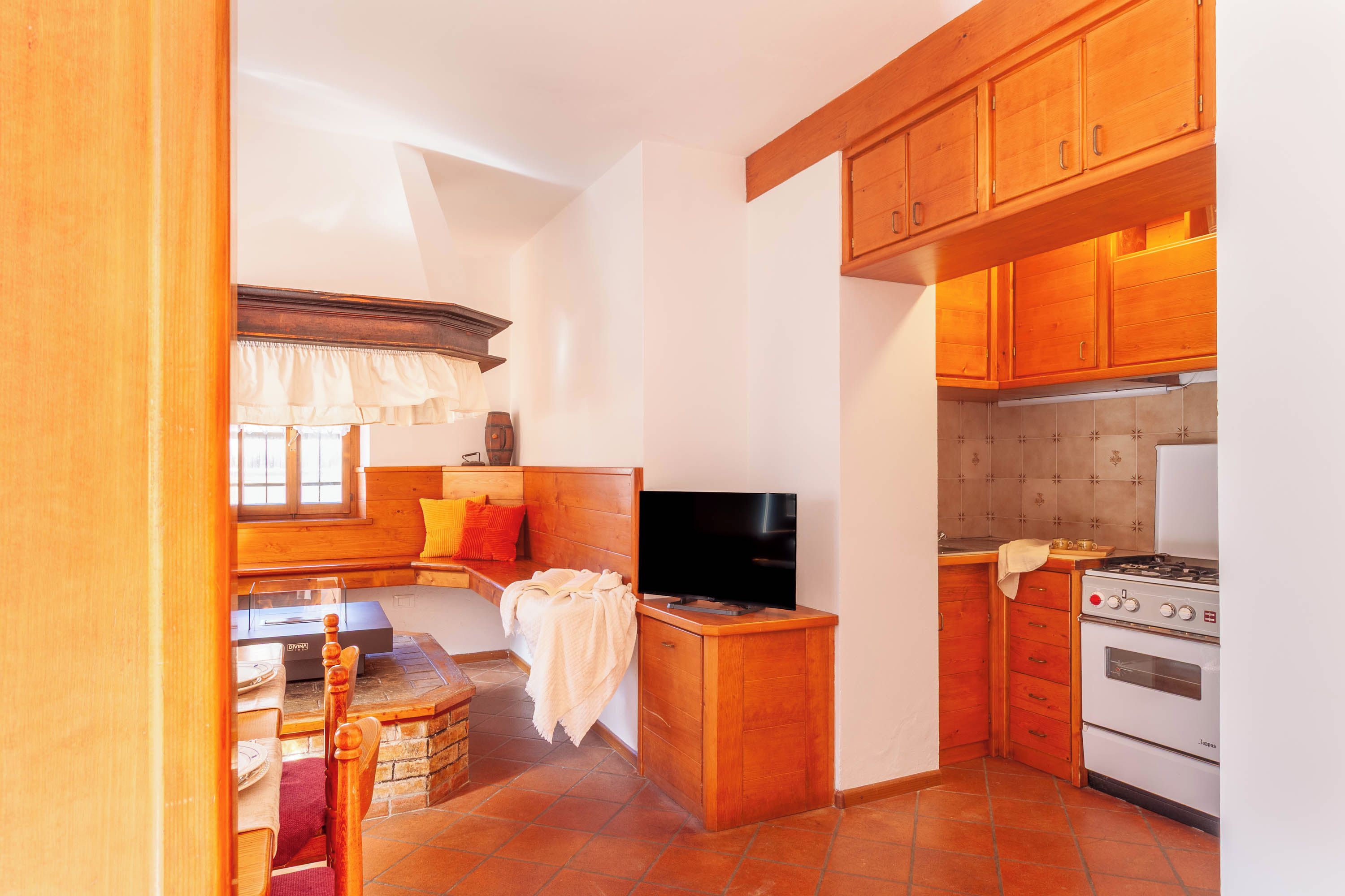 A compact kitchen with wooden cabinets, a stove, and a television.