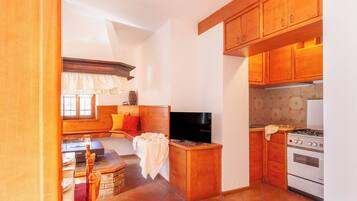 A compact kitchen with wooden cabinets, a stove, and a television.